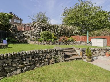 A garden with stone walls and steps surrounded by greenery and plants at Clyd Fan in Harlech