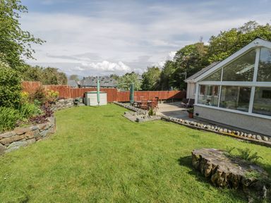 An outdoor garden area with grass lawn stone walls wooden fence and patio with table and chairs at Clyd Fan in Harlech