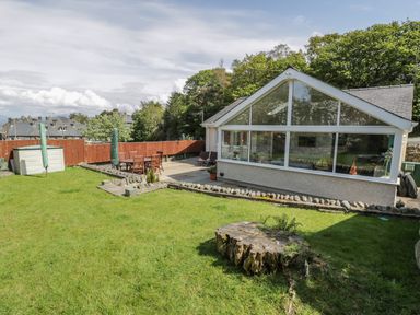 A backyard with a lawn and a patio area with outdoor furniture and umbrellas at Clyd Fan in Harlech