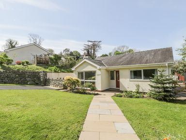 A single story house with a stone walkway leading to the front door surrounded by grass and stone walls at Clyd Fan in Harlech
