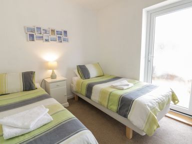 A bedroom with two single beds a nightstand with a lamp and a door with frosted glass at Clyd Fan in Harlech