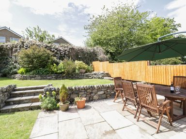 A garden with stone steps and walls wooden table and chairs with an umbrella and plants in pots at Clyd Fan in Harlech