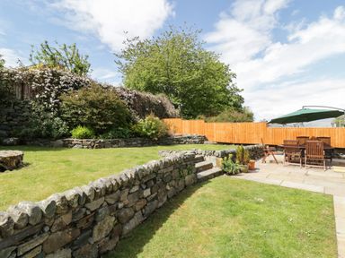 A garden with stone walls wooden fence outdoor dining table and umbrella at Clyd Fan in Harlech