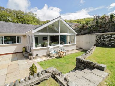 A garden with stone steps and a patio area outside a house with large glass windows at Clyd Fan in Harlech