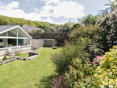 A garden with chairs and a table near a conservatory and a stone wall in the background at Clyd Fan in Harlech