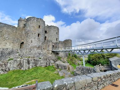 An old stone castle with round towers and a modern metal bridge leading to its entrance