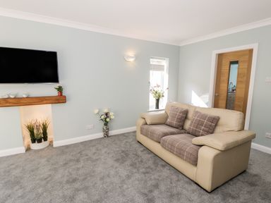 A living room with a beige sofa a wall-mounted TV and plants in Harlech