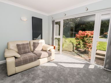 A room with a beige sofa with checkered cushions and a large window showing plants outside at Clyd Fan in Harlech