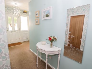 An entrance hallway with a white door a small white table with a vase of flowers a wall mirror and framed pictures at Clyd Fan in Harlech
