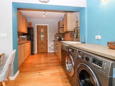 A kitchen with wooden cabinets a washing machine a dishwasher a microwave and a wooden door at Clyd Fan in Harlech