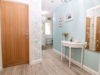 A hallway with a wooden door a white console table with flowers and decorations a large mirror and a white front door at Clyd Fan in Harlech
