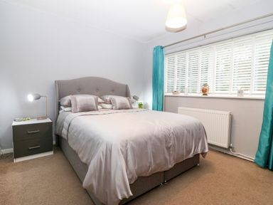 A bedroom with a grey bed and bedside table with lamp by a window with blue curtains at Clyd Fan in Harlech