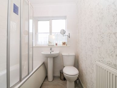 A bathroom with a bathtub and shower screen a sink a toilet a window with a curtain and a radiator on the wall at Clyd Fan in Harlech