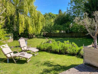 A garden with two lounge chairs on grass and various trees and shrubs at The Old Post Office in Coln St Aldwyns