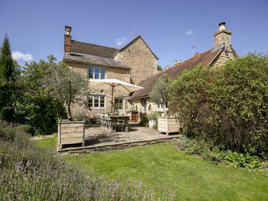 A stone house with a patio table and umbrella in a garden at The Old Post Office in Coln St Aldwyns