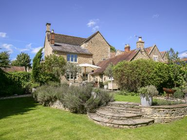 A stone house with a garden patio and greenery at The Old Post Office in Coln St Aldwyns
