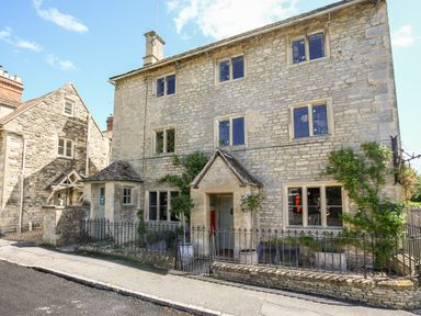 A stone house with multiple windows and a small fenced garden at The Old Post Office in Coln St Aldwyns