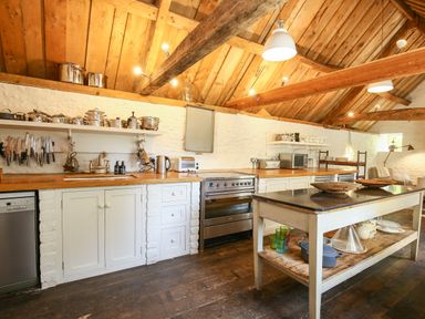 A kitchen with wooden countertops knives hanging on the wall and a central island at The Old Post Office in Coln St Aldwyns