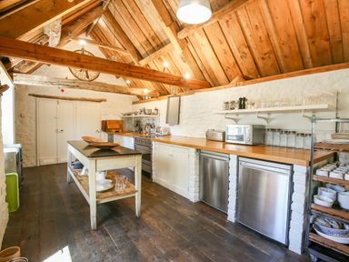 A kitchen with wooden ceiling beams and floors with stainless steel appliances and white cabinets at The Old Post Office in Coln St Aldwyns