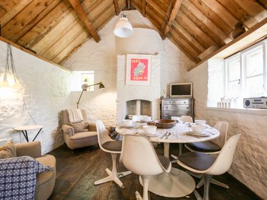 A dining room with a round table set with bowls and cutlery surrounded by chairs with exposed wooden beams at The Old Post Office in Coln St Aldwyns