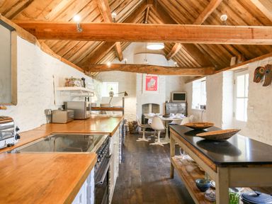 A kitchen with wooden countertops a central island and a dining area with white chairs at The Old Post Office in Coln St Aldwyns
