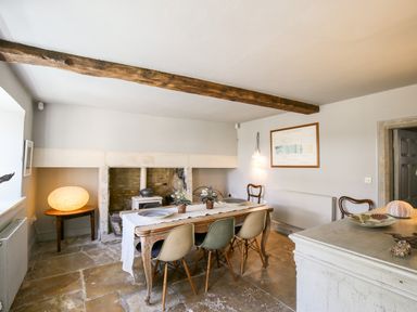 A dining room with a wooden table and chairs and a stone fireplace at The Old Post Office in Coln St Aldwyns