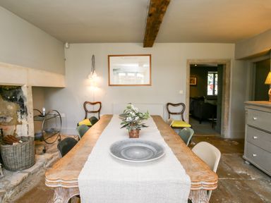 A dining room with a wooden table and chairs near a stone fireplace at The Old Post Office in Coln St Aldwyns