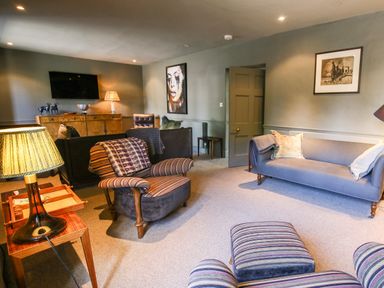 A living room with striped armchairs a gray sofa and wooden furniture at The Old Post Office in Coln St Aldwyns