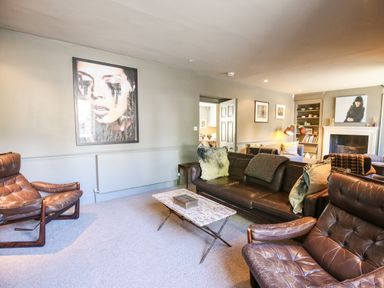A living room with leather chairs a sofa a coffee table a fireplace and wall art at The Old Post Office in Coln St Aldwyns