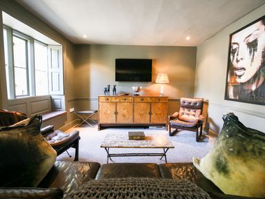 A living room with leather chairs a wooden cabinet and a wall mounted television at The Old Post Office in Coln St Aldwyns