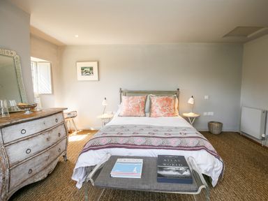 A bedroom with a bed flowers pattern pillows and books on a bench at The Old Post Office in Coln St Aldwyns