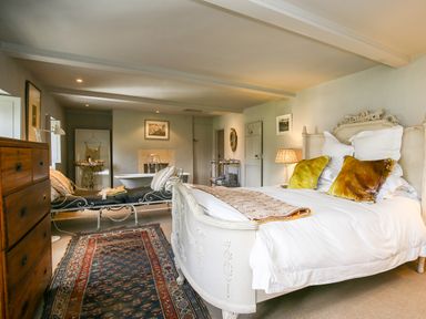 A bedroom with a large bed and pillows a wooden dresser a chaise lounge a rug and a bathtub in the background at The Old Post Office in Coln St Aldwyns