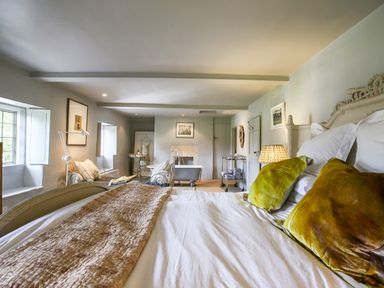 A bedroom with a bed a bathtub two armchairs and windows at The Old Post Office in Coln St Aldwyns