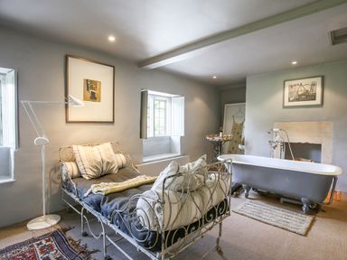 A room with a metal daybed with cushions a floor lamp a clawfoot bathtub and framed pictures on walls at The Old Post Office in Coln St Aldwyns