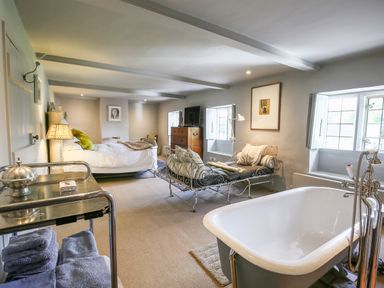 A bedroom with a double bed a chaise lounge a bathtub and a chest of drawers at The Old Post Office in Coln St Aldwyns
