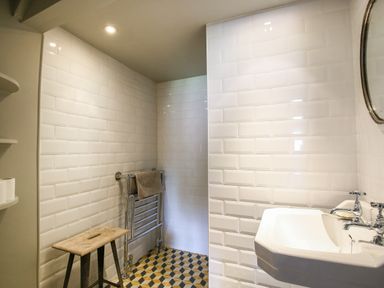 A bathroom with white tiled walls a sink a towel rack with towels and a wooden stool at The Old Post Office in Coln St Aldwyns
