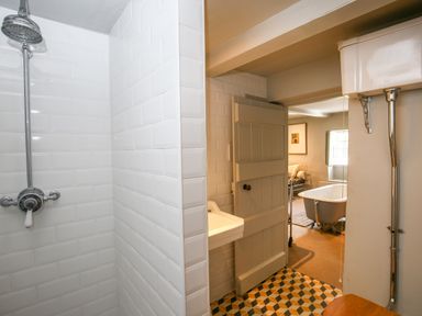 A bathroom with a shower and sink next to a door leading to another room with a bathtub at The Old Post Office in Coln St Aldwyns