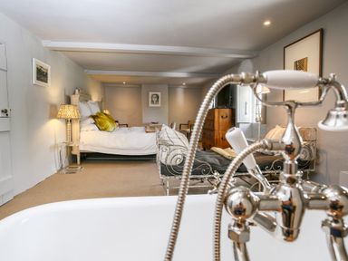 A bedroom with a bed side tables chairs and a bathtub faucet in the foreground at The Old Post Office in Coln St Aldwyns