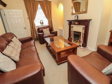 A living room with brown leather sofas a wooden coffee table and a fireplace at Victoria Cottage in Amble