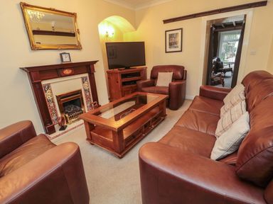 A living room with leather sofas a wooden coffee table a fireplace and a television at Victoria Cottage in Amble