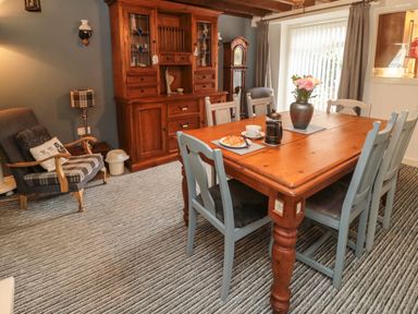 A dining room with a wooden table set with chairs a flower vase and a cabinet against the wall at Victoria Cottage in Amble