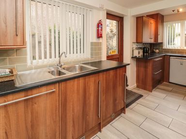 A kitchen with wooden cabinets a double sink a countertop a kettle and a door with windows at Victoria Cottage in Amble