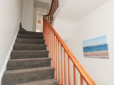 A carpeted staircase with wooden handrail and a wall painting of a coastal scene at Victoria Cottage in Amble