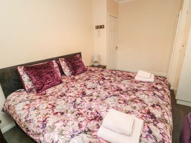 A bedroom with a double bed covered with floral bedding and two folded towels at Victoria Cottage in Amble