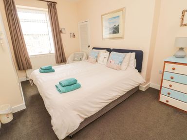 A bedroom with a double bed with pillows and folded towels near a window and a chest of drawers at Victoria Cottage in Amble