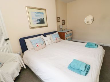 A bedroom with a double bed blue and white pillows folded towels on bed dresser with lamp and decorations at Victoria Cottage in Amble