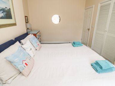 A bedroom with a double bed white pillows turquoise towels wooden chest of drawers and a framed picture at Victoria Cottage in Amble