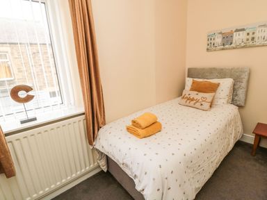 A small bedroom with a single bed with cushions and folded towels next to a window at Victoria Cottage in Amble