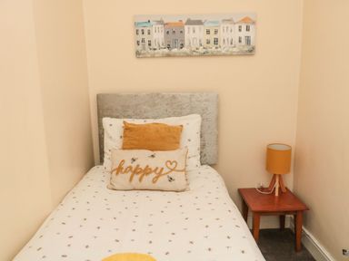 A single bed with pillows and a bedside table with a lamp in a bedroom at Victoria Cottage in Amble