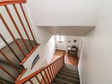 A staircase with wooden handrails leading down to an entryway with a white door and a small wooden table at Victoria Cottage in Amble